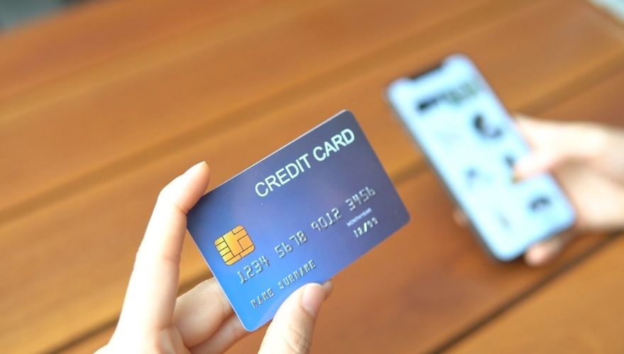 Person holding a credit card while checking account information on a smartphone.