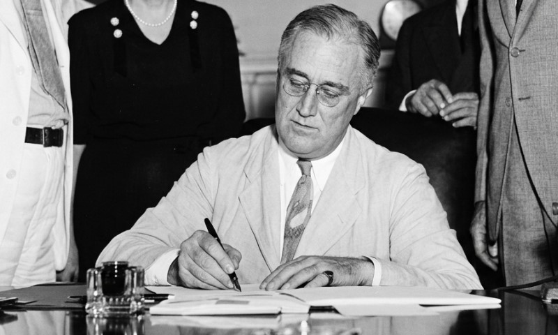 Franklin D. Roosevelt signs a document at a desk