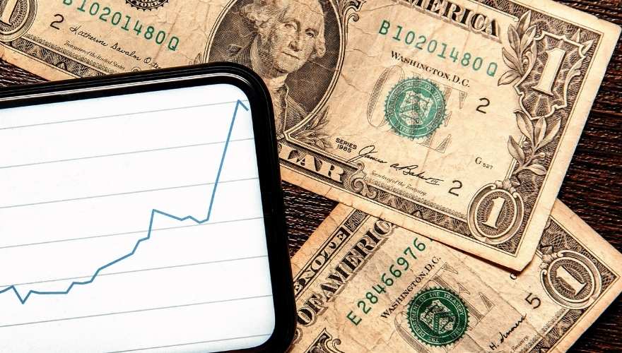 Old US dollar bills next to a smartphone displaying an upward-trending graph, illustrating the increasing value of savings bonds over time.