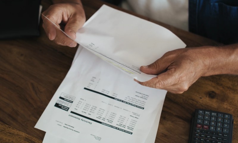 Hands hold a paper check above a printed financial statement on a wooden desk