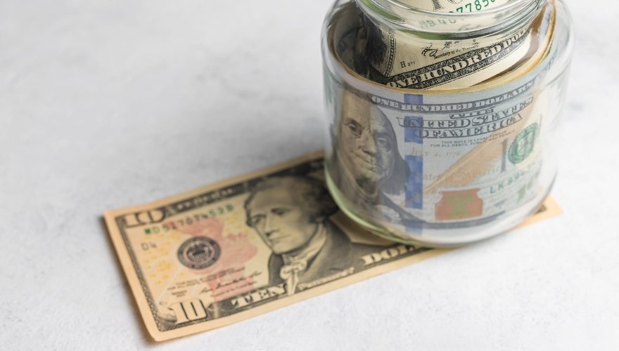 Glass jar filled with US dollar bills resting on a ten-dollar bill, illustrating savings bonds and long-term money savings.